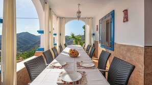 Une longue table à manger, dressée pour six personnes, avec des chaises en osier, un lustre et une vue sur les montagnes.