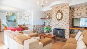 Un salon avec une cheminée, un téléviseur et un ensemble de meubles (canapé, fauteuils, etc.).