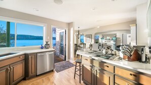 A modern kitchen with a large island, stainless steel appliances, and a view of a lake. - Erlands Point Beach House (Bremerton)