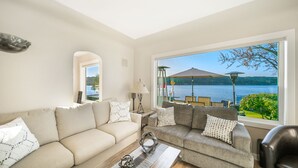 A living room with a large window overlooking a lake, furnished with two sofas and a coffee table. - Erlands Point Beach House (Bremerton)
