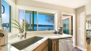 A kitchen with a large window, a sink, a coffee maker, and a dishwasher. - Erlands Point Beach House (Bremerton)