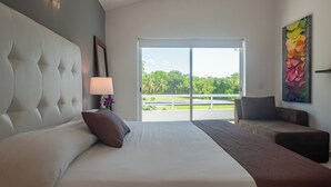 Ein Hotelzimmer mit einem großen Bett, einer Sitzecke, einem Balkon mit Blick auf Grünflächen und einem Bild an der Wand.
