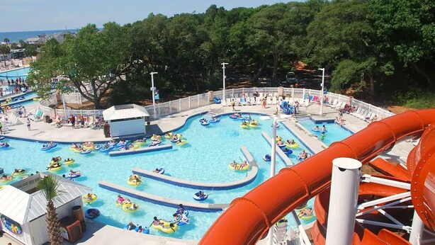 A water park with multiple pools, a large water slide, and a fenced area with lounge chairs. - Site M66 Lakeview 3BR Golf Cart | Walk to Beach/Waterpark | (Myrtle Beach)