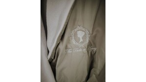 En närbild på ett beige tyg med ett broderat monogram och text.
