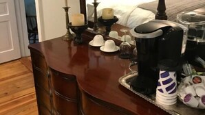 En byrå i trä med en spegel, en lampa och diverse föremål ovanpå, inklusive en kaffebryggare, koppar och ett bricka med tallrikar.