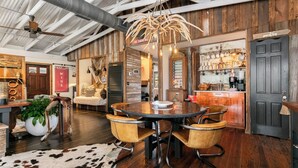 Un intérieur rustique avec une table ronde, deux chaises, un lustre et un coin bar agrémenté d’un panneau « Il est interdit de fumer ».