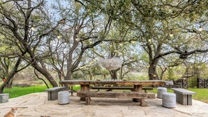 Un espace extérieur aménagé avec un banc en bois, des tables en pierre et un élément décoratif central.