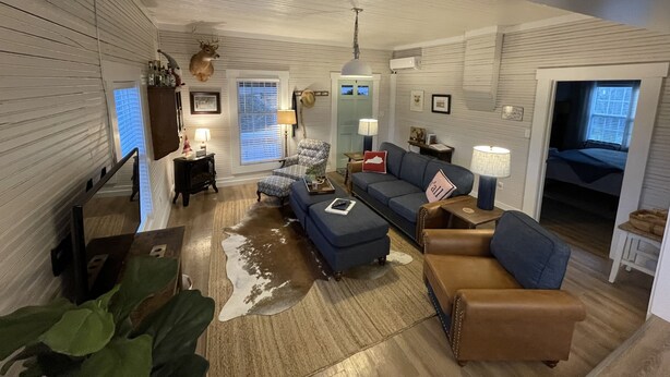 A spacious living room with a large sofa, a brown leather chair, and a blue armchair. There is a wooden floor, a white ceiling, and a window with blinds. - Bourbon Trail & Relaxing rural spot. Restored Farmhouse on 22 private acres. (Lawrenceburg)