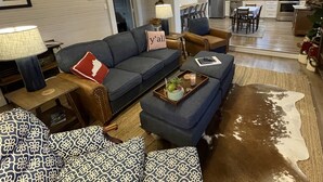 A living room with a sofa, ottoman, and a cowhide rug. There is a dining area with a table and chairs. - Bourbon Trail & Relaxing rural spot. Restored Farmhouse on 22 private acres. (Lawrenceburg)