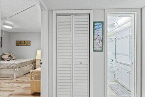 A bedroom with a bed, a bedside table, a wall-mounted lamp, a closet, and a bathroom visible through an open door.