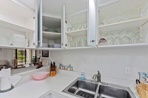 Une cuisine moderne avec des meubles blancs, un évier en acier inoxydable et un plan de travail agrémenté d’un saladier rose.