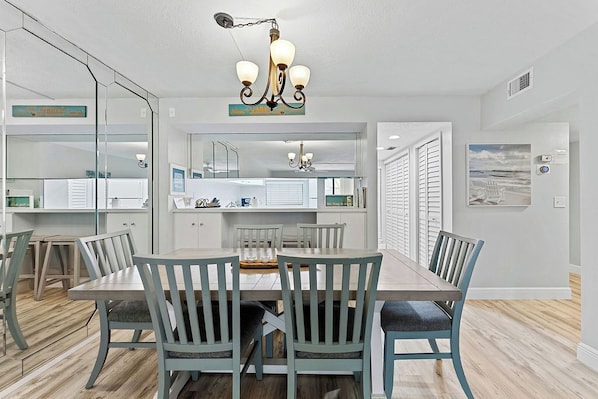 A dining area with a wooden table and chairs, a chandelier, and a view of the kitchen through a glass partition. - Siesta Escape - Ground Floor 2 BR 2 BA - on Inter-coastal and Free Trolley Stop (Siesta Key)