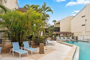 A pool area with lounge chairs, palm trees, and a building with balconies. - Siesta Escape - Ground Floor 2 BR 2 BA - on Inter-coastal and Free Trolley Stop (Siesta Key)