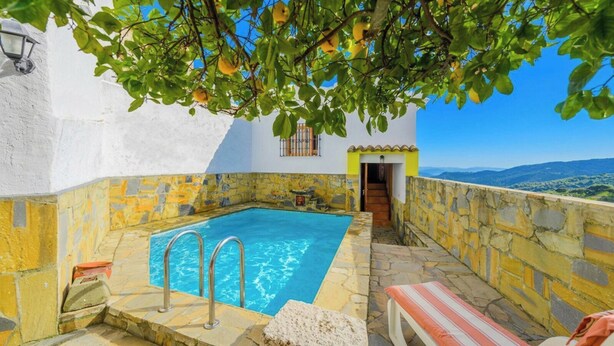 Une piscine aux murs de pierre, un bâtiment blanc et une vue sur le paysage.