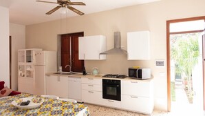 Una cocina funcional con gabinetes blancos, estufa a gas, microondas y ventilador de techo.