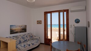 Quarto com uma mesa de madeira, um sofá estampado, um quadro e vista para a praia através de uma porta.