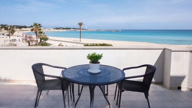 Mesa redonda con dos sillas y una planta en maceta en un balcón con vistas a la playa.