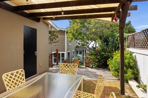 Eine überdachte Terrasse mit einem Glastisch und gelben Stühlen, umgeben von Topfpflanzen und einem Holzboden.