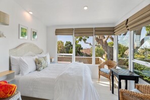 Ein Schlafzimmer mit einem großen Bett, einem Sessel, einem Tisch und Blick ins Freie.