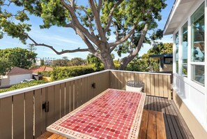 Eine Holzterrasse mit einem roten Tisch und Stühlen, umgeben von einem weißen Zaun und einem großen Baum.