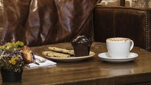 A cozy seating area with a leather couch, a table with a cup of coffee and pastries, and a wall with a framed collage of papers. - Meroddi Galata Mansion (Istanbul)