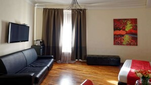Une chambre d’hôtel avec un canapé en cuir noir, un lit recouvert d’une courtepointe à rayures rouges et blanches, un téléviseur à écran plat, une petite table avec une lampe et un tableau accroché au mur.