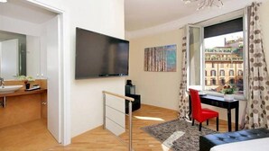 Une chambre d’hôtel moderne avec un plancher en bois, un lit, un bureau avec une chaise, une télévision, une fenêtre avec des rideaux et un tableau au mur.