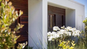 A modern house with a white exterior, wooden window frames, and a garden with white flowers. - Secluded Luxury (Greens Beach)