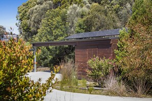 A modern building with a sloped roof, surrounded by dense vegetation and a clear sky.