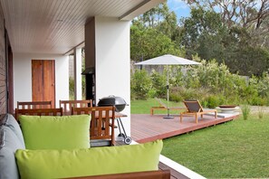 A patio with a wooden deck, outdoor furniture, and a grill.