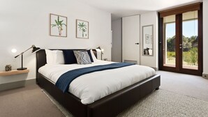 A modern bedroom with a large bed, a nightstand, a lamp, and two framed botanical prints on the wall. - Secluded Luxury (Greens Beach)