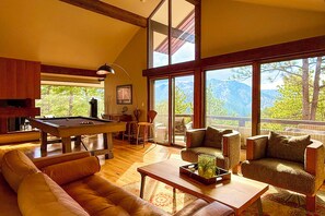 Amplia sala de estar con mesa de billar, asientos cómodos y grandes ventanales con vistas a la montaña.