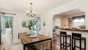 A dining area with a wooden table and chairs, a chandelier, and a view of the kitchen and outdoor space. - Downtown SB Cottage! Charming Cozy and Recently Remodeled (Santa Barbara)
