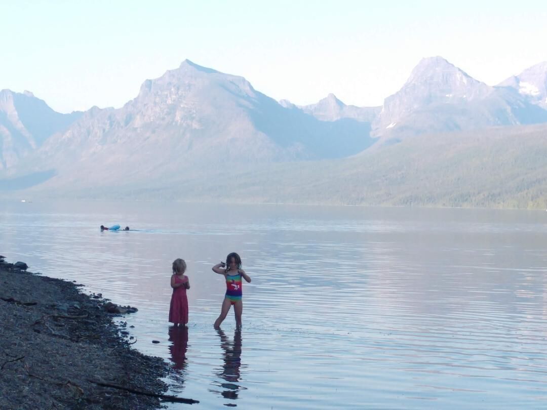 Ein See mit Bergen im Hintergrund und zwei spielenden Kindern im Wasser.