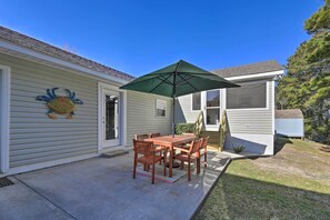 A patio with a wooden table and chairs, a green umbrella, and a crab decoration on the wall. - Beaufort Pad w/ Patio: 3 Blocks to Waterfront! (Beaufort)