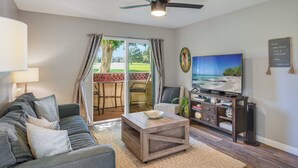 Una sala de estar con sofá, mesa de centro, televisor y vista a un patio con mesa y sillas.