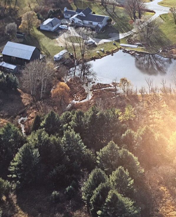 An aerial view of a residential area with houses, a pond, and surrounding trees.