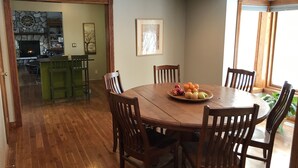A dining area with a wooden table and chairs, a fruit bowl, and a view of a kitchen with a stone fireplace.