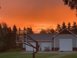 A garage with a boat and a basketball hoop in front.