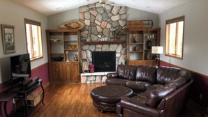 A living room with a stone fireplace, leather sofa, wooden cabinets, and a television.