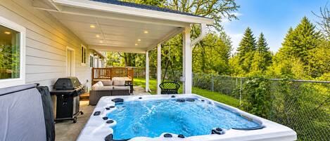 Un bain à remous situé dans un espace extérieur abrité, avec une terrasse, un barbecue et un coin salon.
