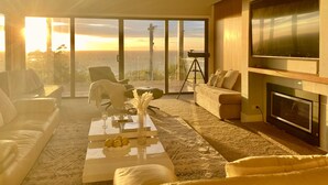 A spacious living room with a large TV, comfortable seating, a fireplace, and a balcony with a view of the sunset. - Mount Martha Oceanfront Retreat | Pool, Spa, Views | Pet & Family Friendly (Mount Martha)