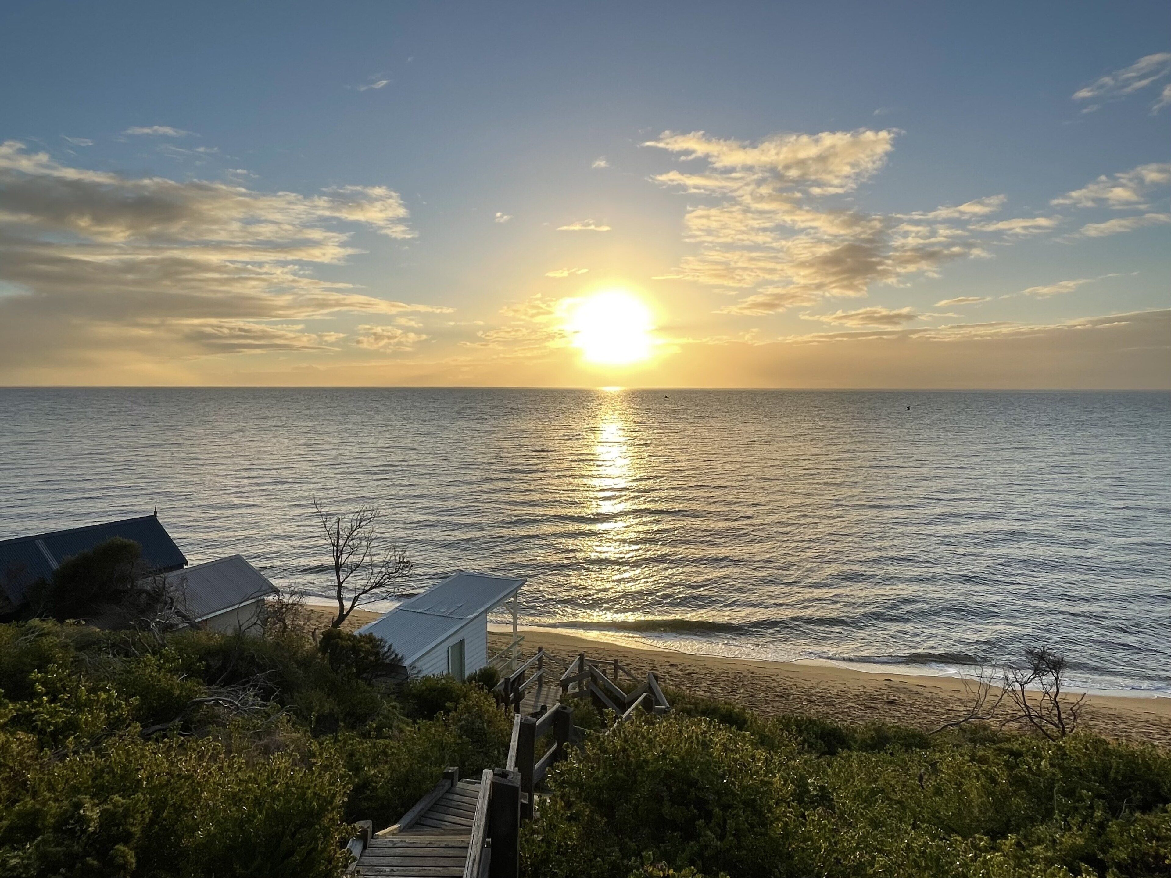 En strand med en trægangsti, der fører til en mindre bygning, med udsigt over havet i solnedgang.