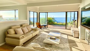 A modern living room with a beige sofa, a coffee table, and a chair. There is a large window with a view of the ocean. - Mount Martha Oceanfront Retreat | Pool, Spa, Views | Pet & Family Friendly (Mount Martha)