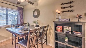 Un comedor con una mesa de madera, sillas, un ventilador de techo, un reloj y una estantería con un letrero de 'Wi-Fi'.