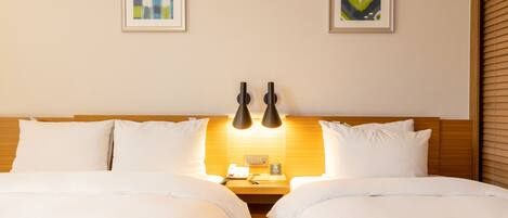 A double bed with white bedding, two bedside tables, a wall-mounted lamp, and two framed artworks on the wall.