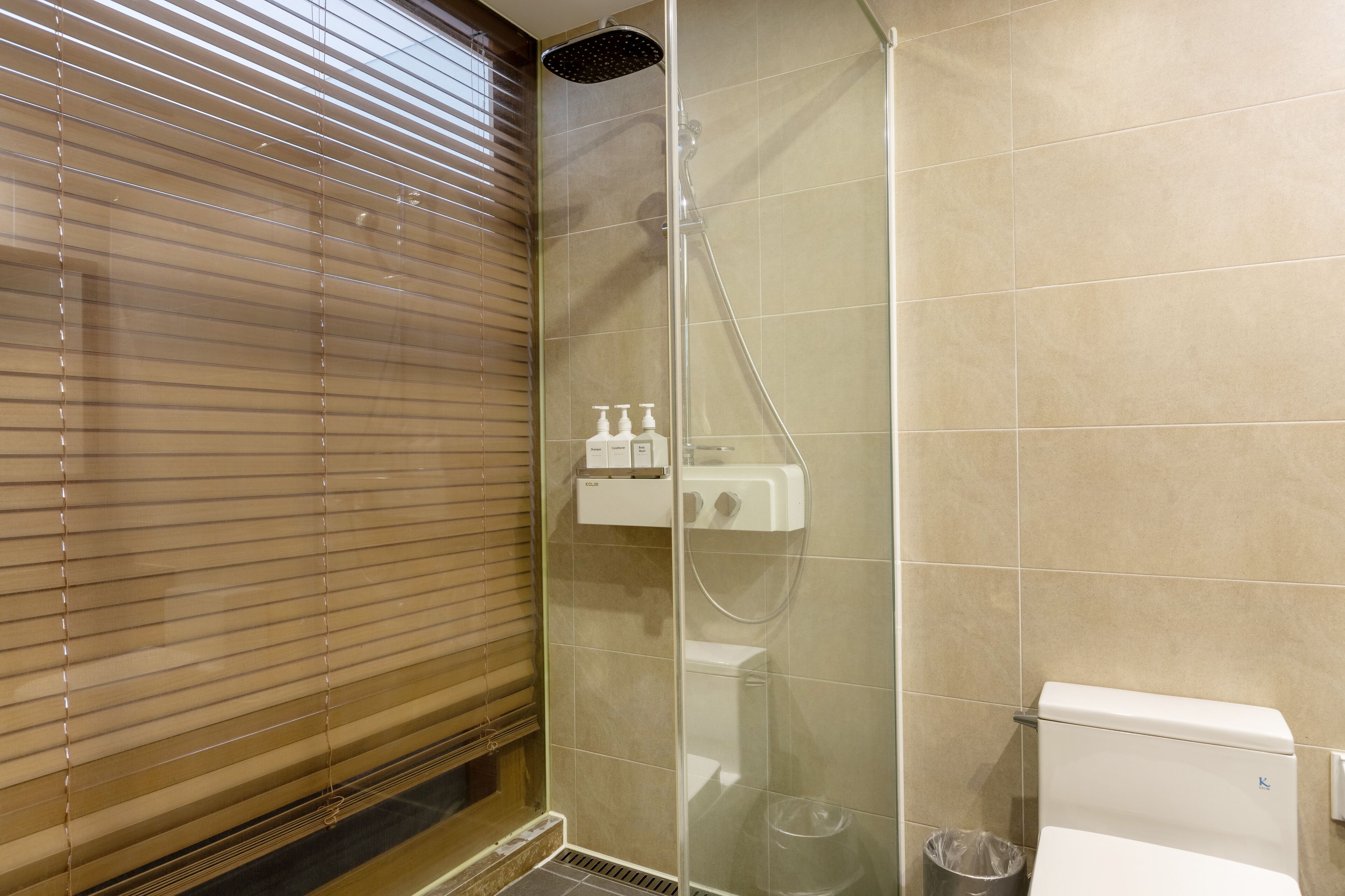 A bathroom with a shower, toilet, and window with blinds.