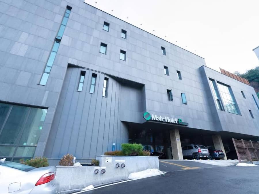 A modern hotel building with a flat facade, large windows, and a parking area with cars.