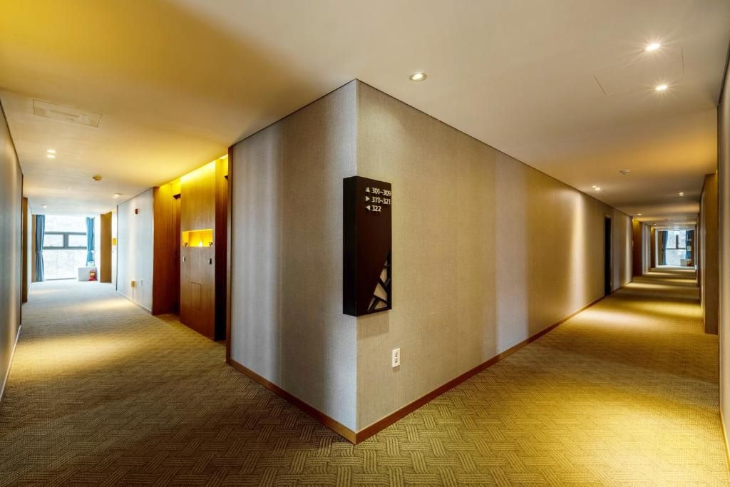 Un pasillo de hotel con piso alfombrado, un directorio en la pared y una puerta a la izquierda.