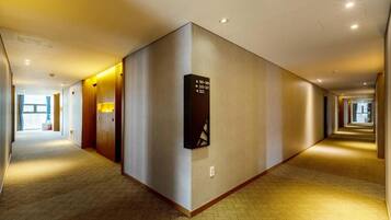 Un pasillo de hotel con piso alfombrado, un directorio en la pared y una puerta a la izquierda.
